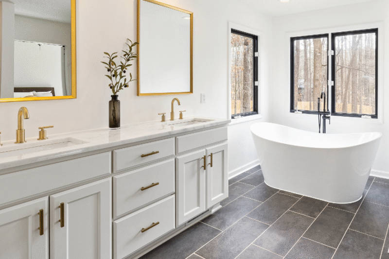Modern Ringwood bathroom renovation by a local builder featuring sleek stone benchtops, gold fixtures, double vanity, and a freestanding bathtub.